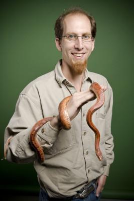 Man in glasses and brown shirt holding a brown snake